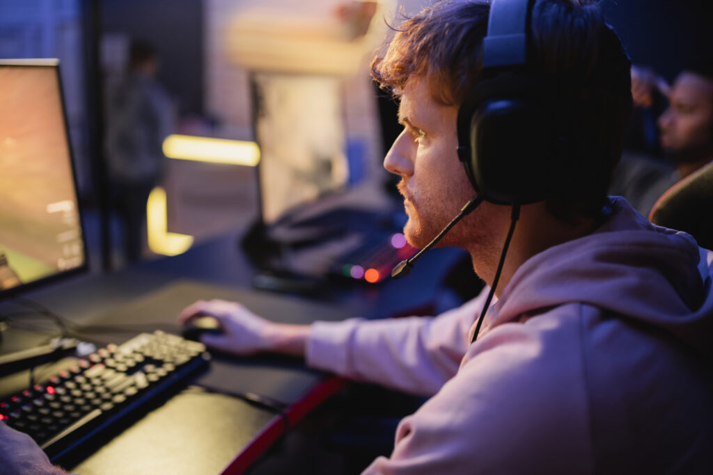 Side view of focused gamer in headphones playing video game on computer in gaming