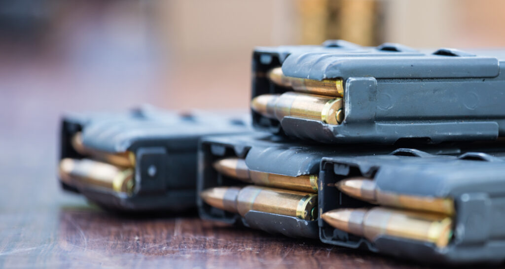 Blue magazines with bullets of firearm putted on wooden table. Ammunition for protection of soldiers. Close up view, blurred background.